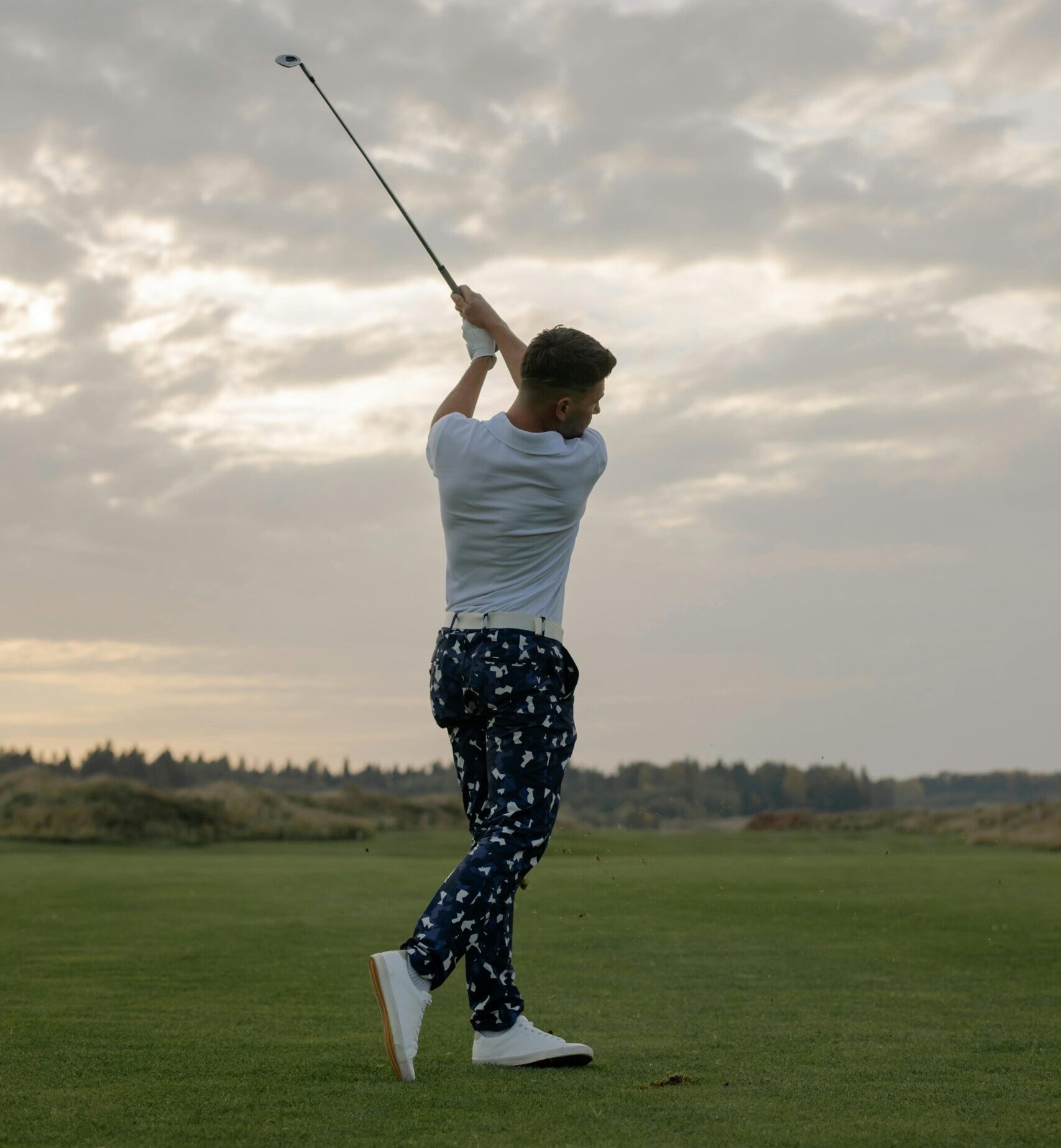 A golfer performing a powerful swing on a lush golf course at sunset.